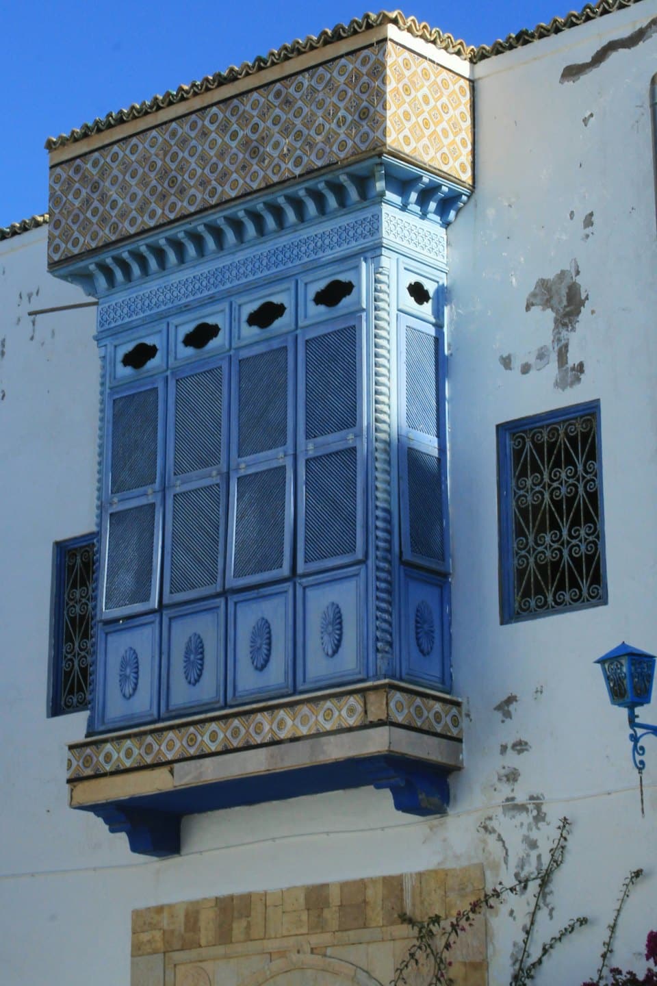 Finestra a bovindo in legno blu ornata su un edificio in intonaco bianco.