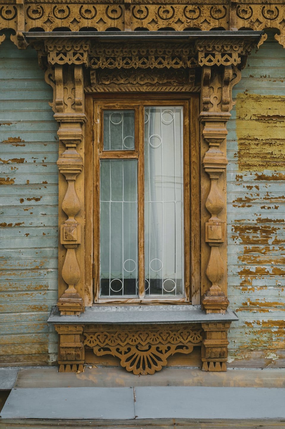 Cornice di legno consumata dal tempo con balaustri intagliati su una facciata blu di scandole.
