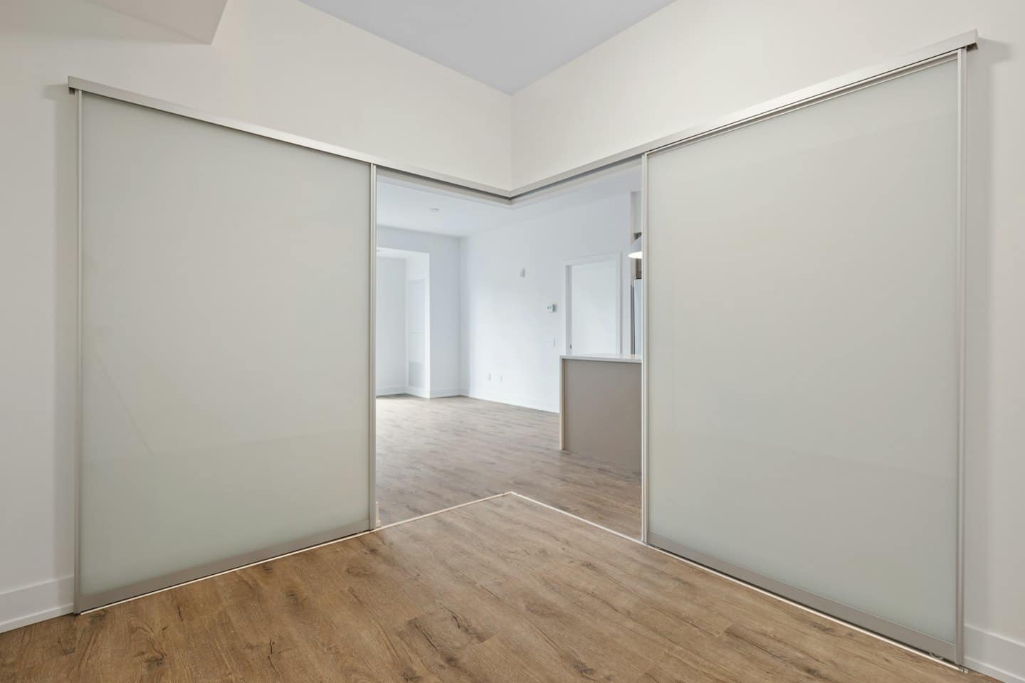 Due porte in vetro satinato aperte rivelano una stanza moderna vuota con un bancone da cucina.